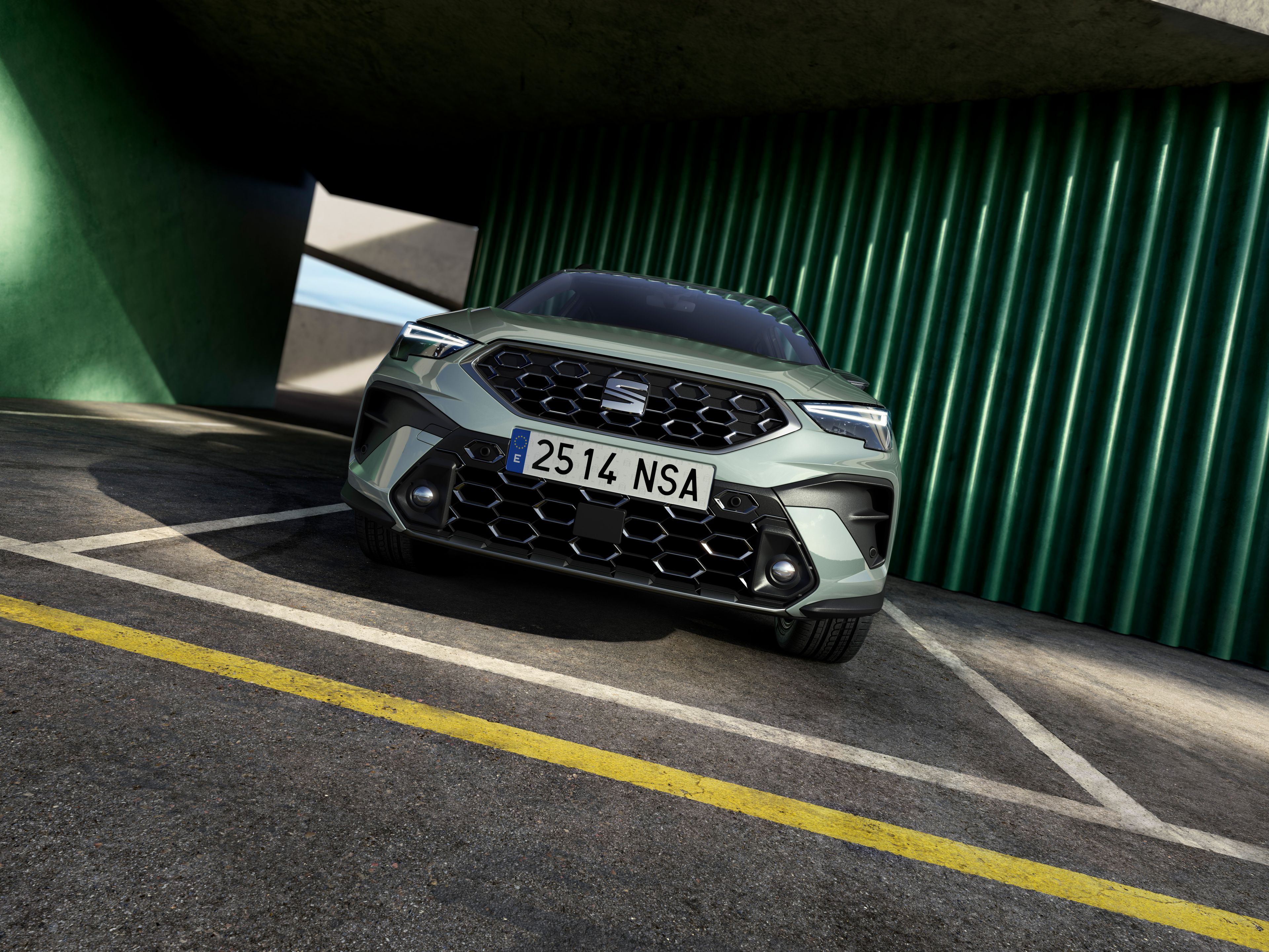 SUV Seat stojaci v modernej garáži ohraničenej zelenými stĺpmi a betónovými rampami. Fotografia je nasnímaná z nízkeho uhla, zvýrazňujúc prednú časť vozidla.