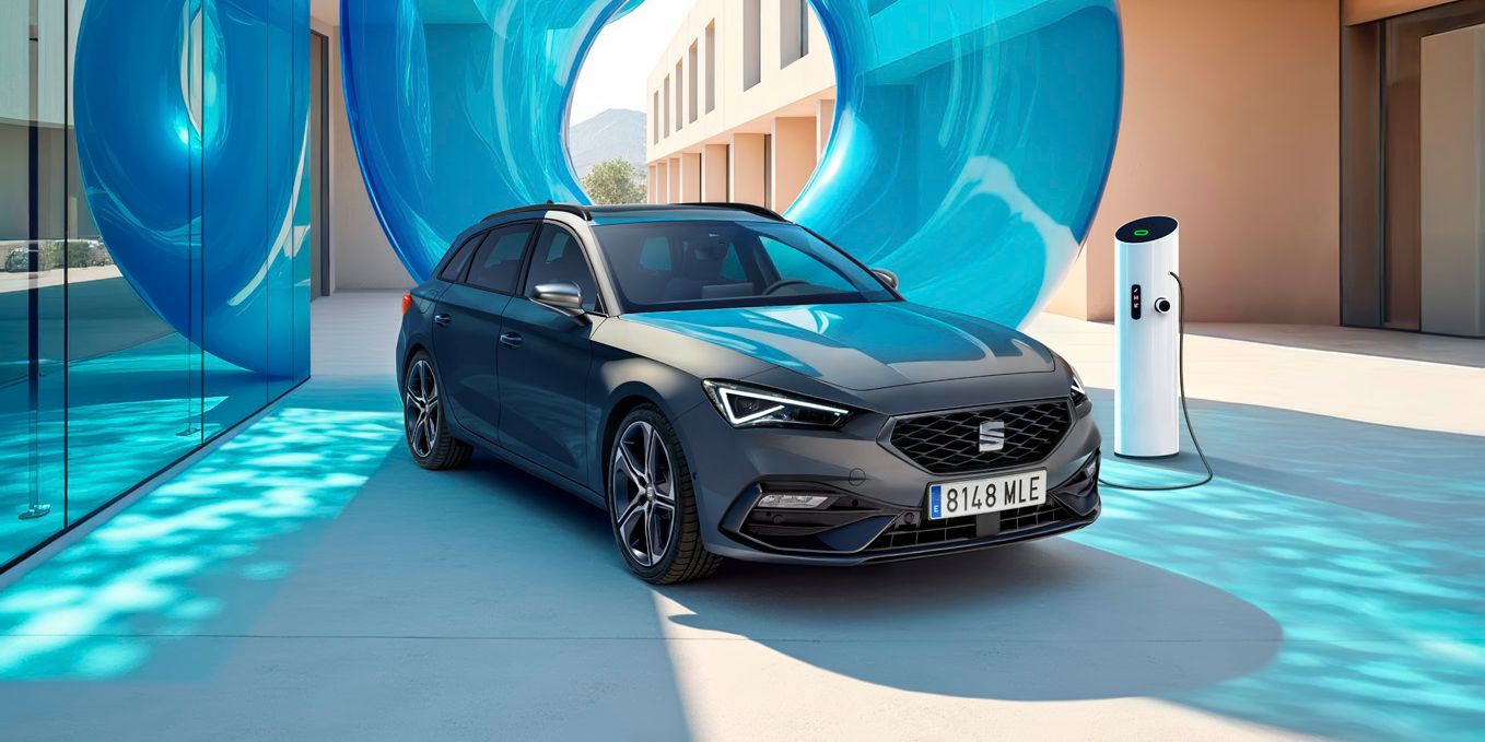 SEAT Leon sa nabíja pri modernej bytovke z jednej strany s presklenou stenou a modrou priehľadnou inštaláciou za ním.