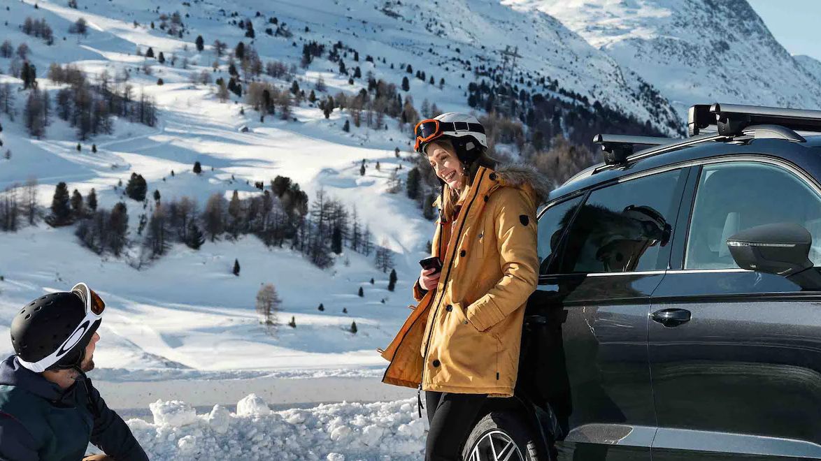 SEAT Ateca stojí pred chalupou v zimnej, zasneženej krajine. Žena v lyžiarskom oblečení sa opiera o vozidlo, muž čupí a pozerá sa na ženu. Rozprávajú sa spolu.
