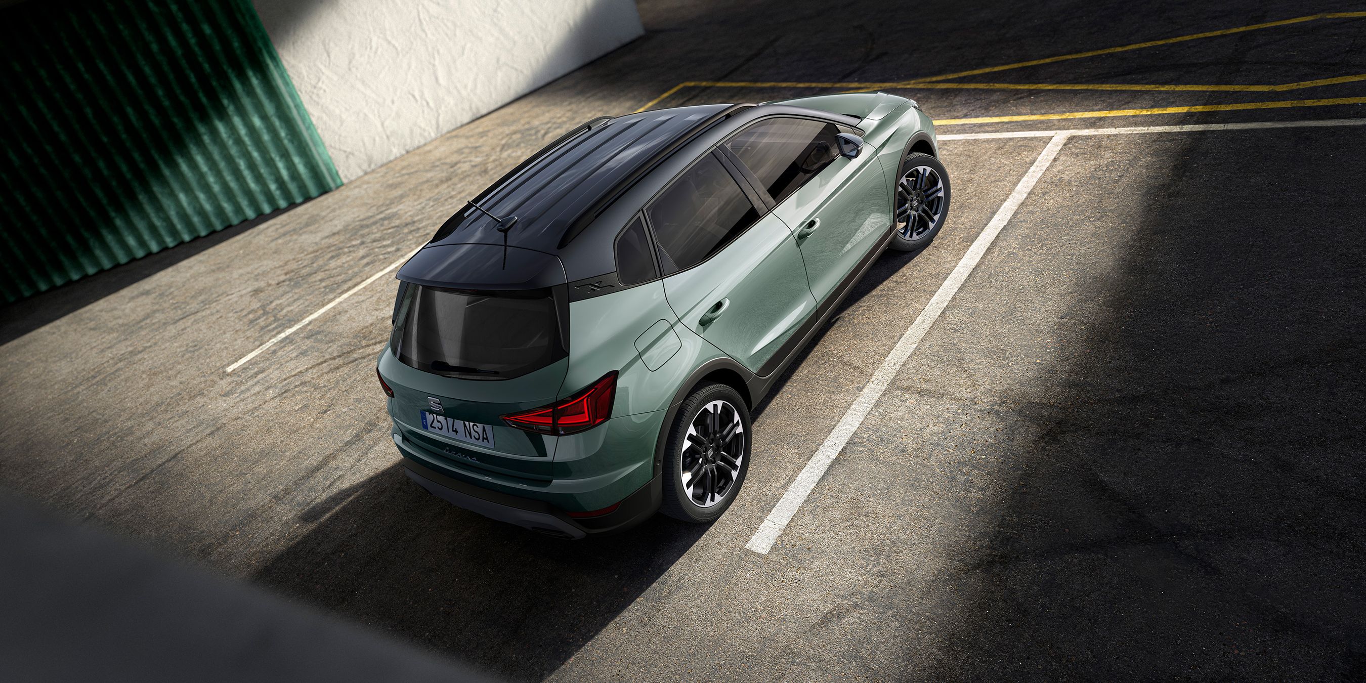 Auto zaparkované na parkovisku, osvetlené slnečnými lúčmi. Svetlozelený automobil s čiernou strechou. Textúra asfaltu je zreteľne viditeľná.