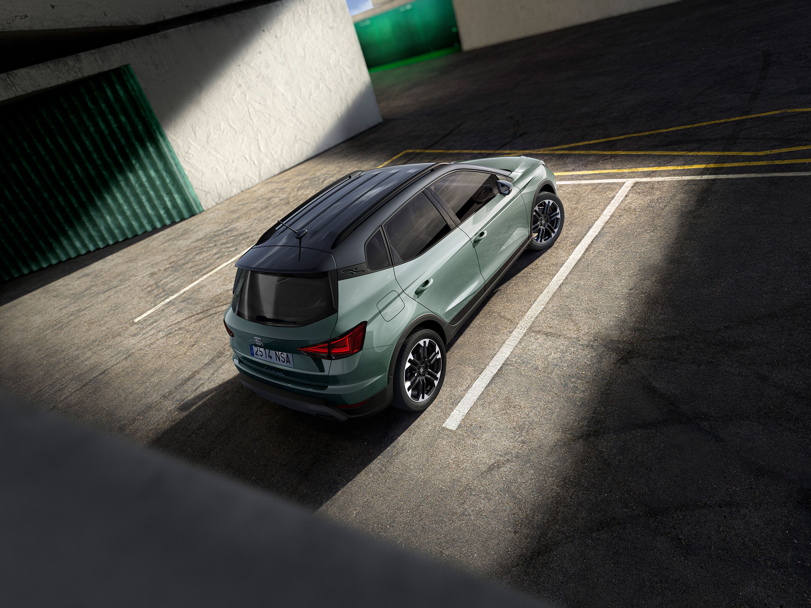 Auto zaparkované na parkovisku, osvetlené slnečnými lúčmi. Svetlozelený automobil s čiernou strechou. Textúra asfaltu je zreteľne viditeľná.