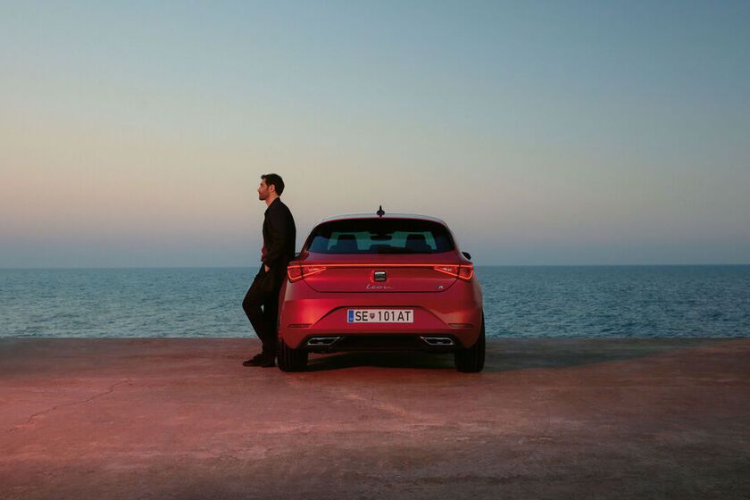 Červený SEAT Leon zaparkovaný na parkovisku v prístave. O vozidlo sa opiera muž. Pred ním je vidieť len more a nebo pri západe slnka.