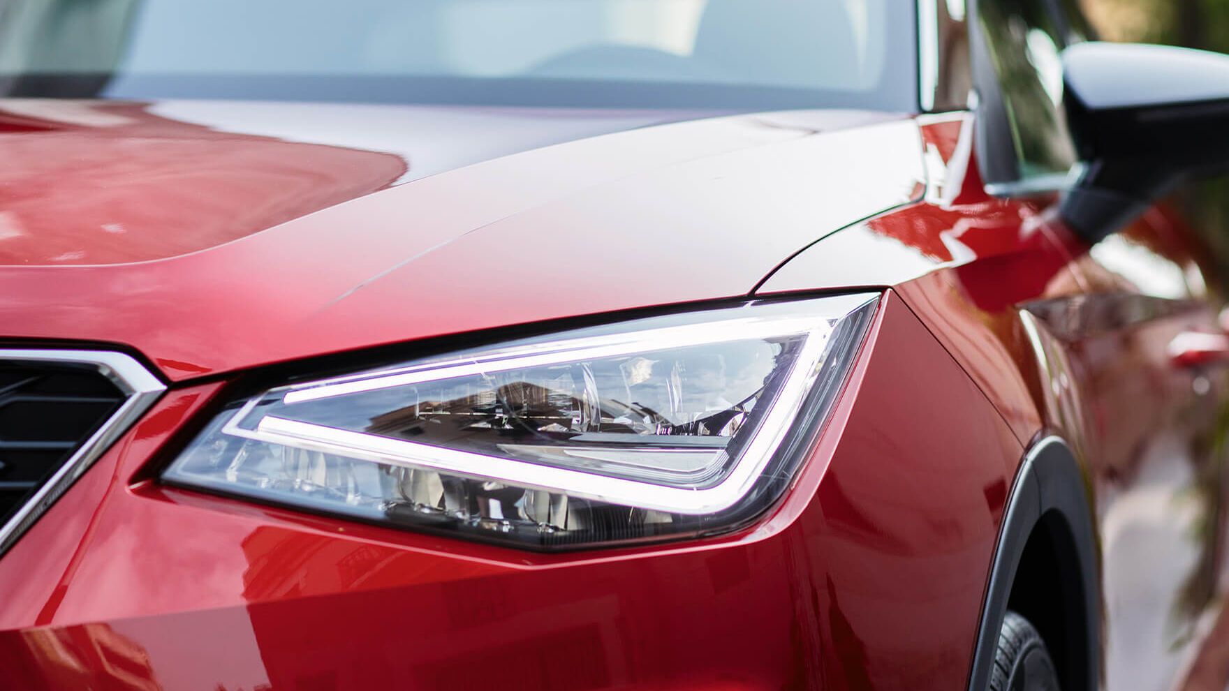 Pohľad na predné partie vozidla SEAT s detailom na predný svetlomet. Za vozidlom vidieť stromy v parku.