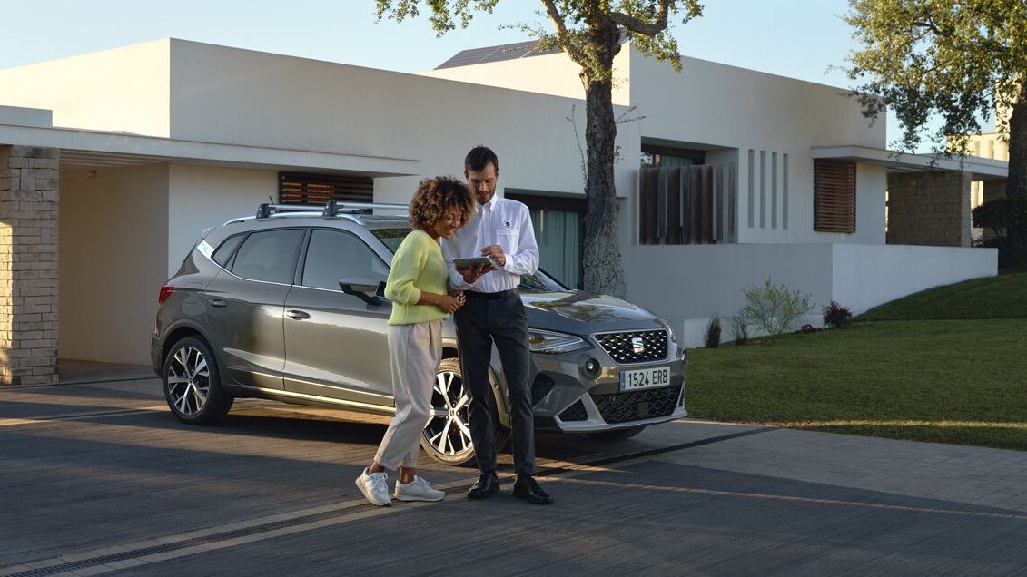 SEAT Arona je zaparkovaný pred modernou vilou. Pri vozidle stoji dvojica, muž a muž ukazuje žene niečo na tablete.