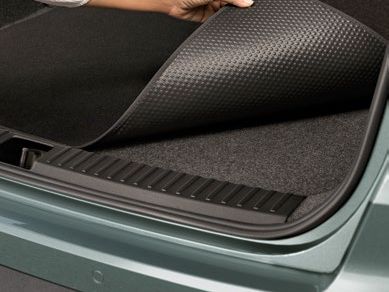 Osoba dvíha gumenú rohož v batožinovom priestore. Rohož má vzor malých bodiek. Interiér batožinového priestoru je tmavo šedý.