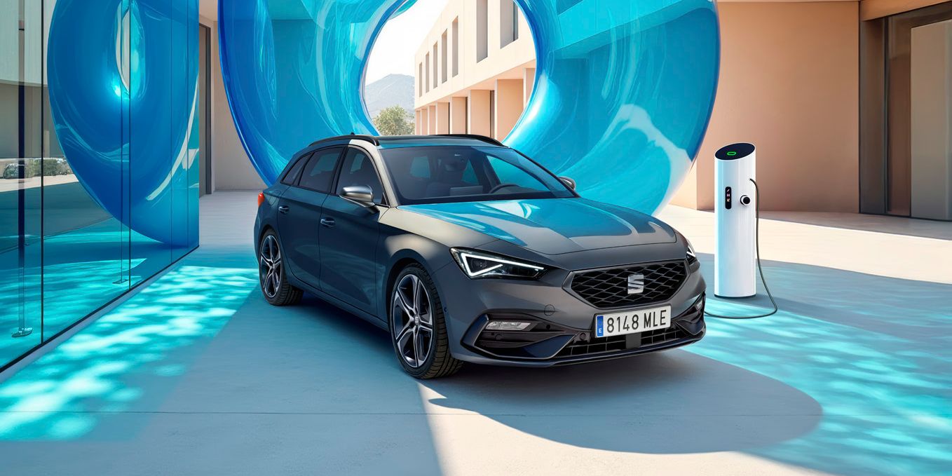 SEAT Leon sa nabíja pri modernej bytovke z jednej strany s presklenou stenou a modrou priehľadnou inštaláciou za ním.