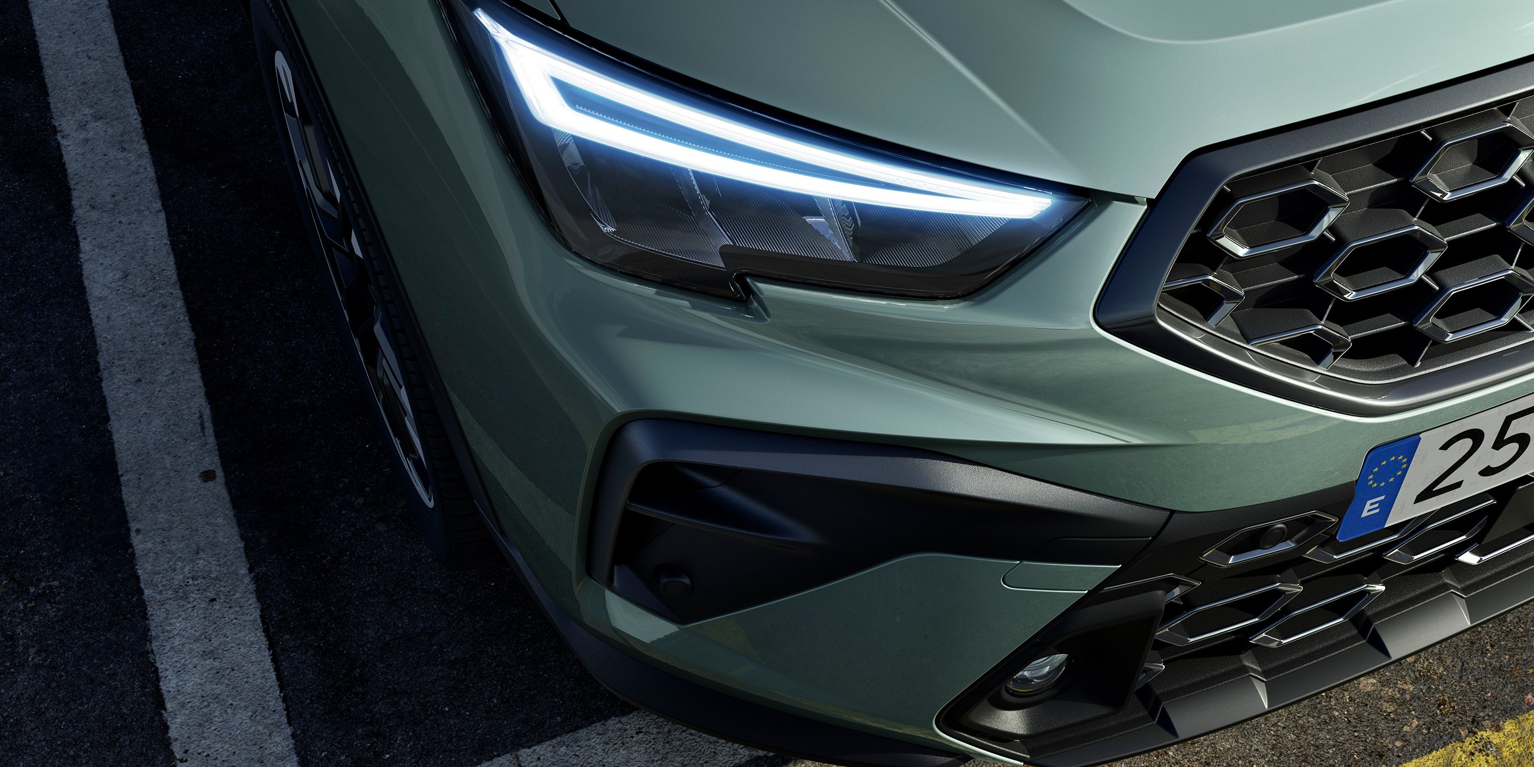 Predná časť zeleného vozidla s modernými LED svetlami. Viditeľná je časť masky chladiča a detail predného nárazníka. Auto je zaparkované na asfaltovom povrchu s vodorovnými čiarami.