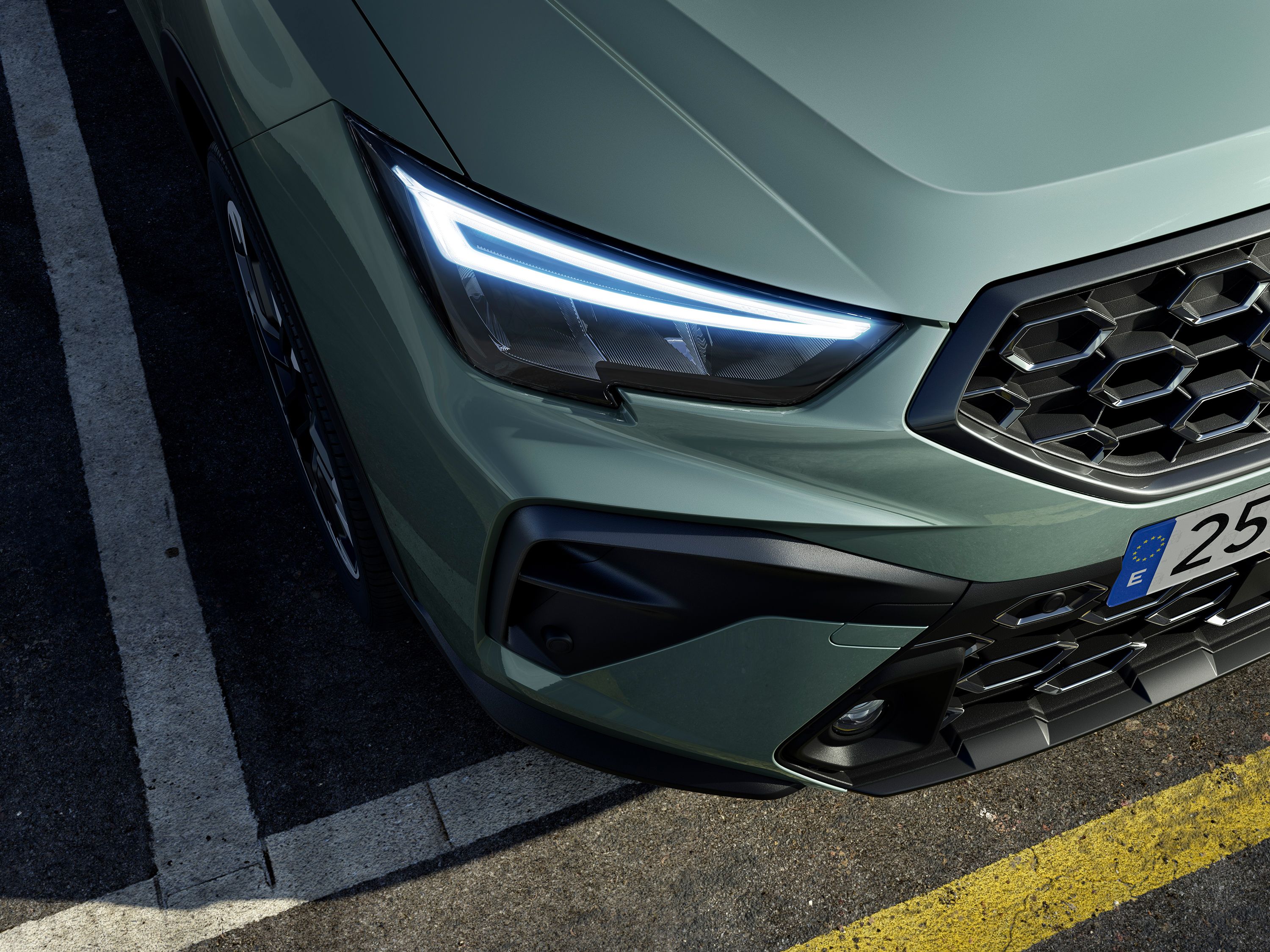 Predná časť zeleného vozidla s modernými LED svetlami. Viditeľná je časť masky chladiča a detail predného nárazníka. Auto je zaparkované na asfaltovom povrchu s vodorovnými čiarami.