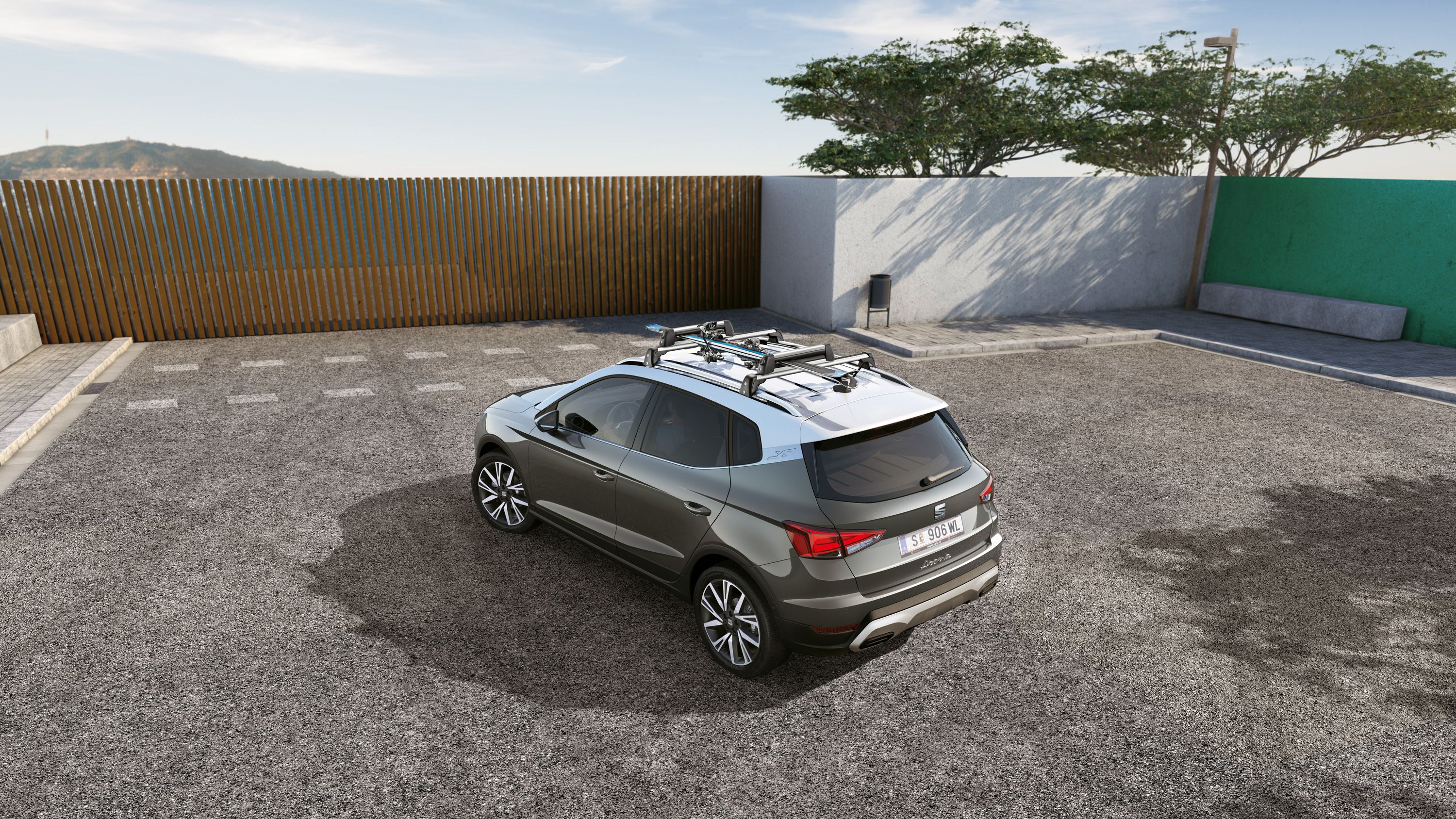 SEAT Arona stojí pred drevenou bránou. Na strešných lištách má upevnený nosič na lyže s lyžami.
