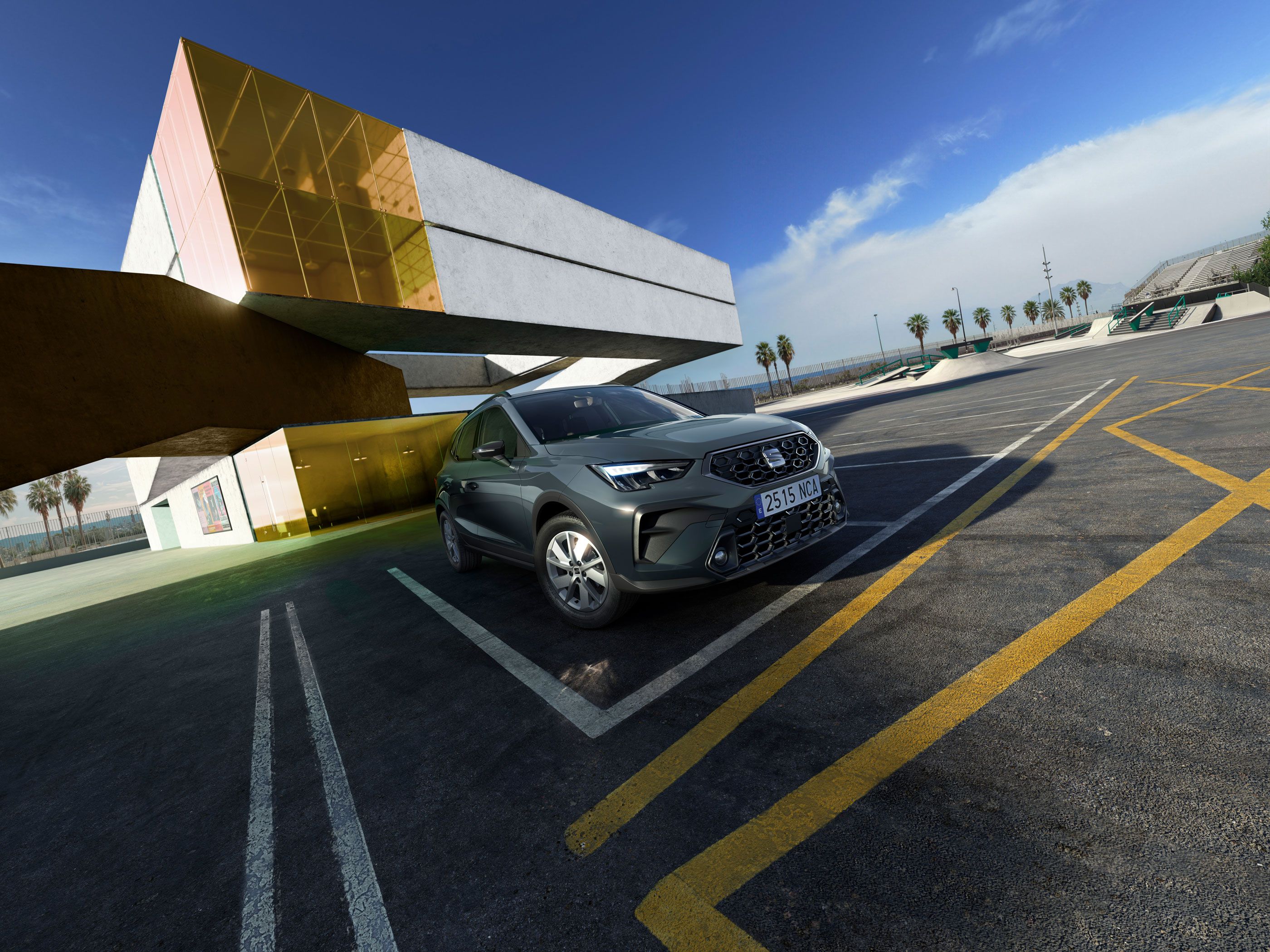 Na obrázku je SUV zaparkované na prázdnom parkovisku. V pozadí je moderná budova so žltými sklenenými stenami. Na okraji parkoviska sú palmy.