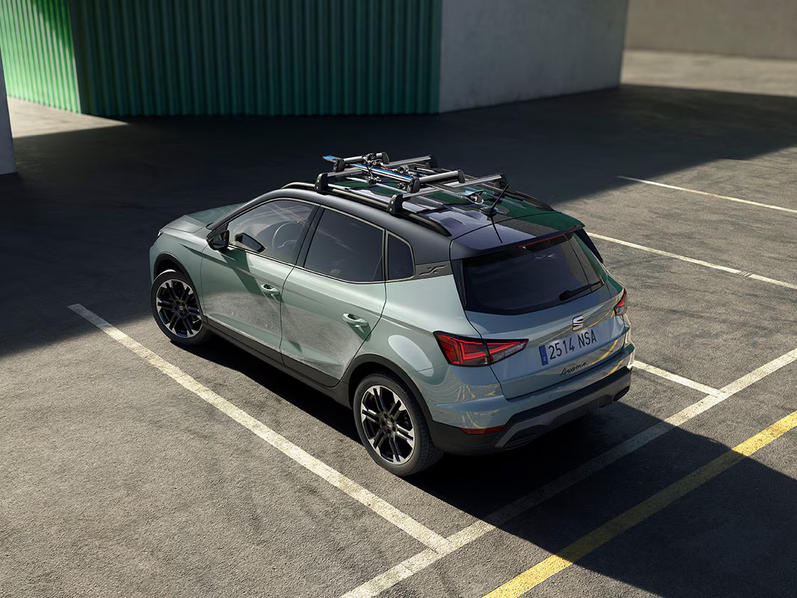 SEAT Arona s nosičom bicyklov na streche je zaparkovaný na parkovisku. Pred vozidlom vidieť časť budovy.