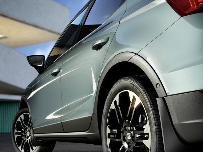 Automobil zaparkovaný na slnečnom mieste so zameraním na zadné koleso a časť karosérie. Koleso má čierne disky s moderným dizajnom. V pozadí je viditeľná budova.