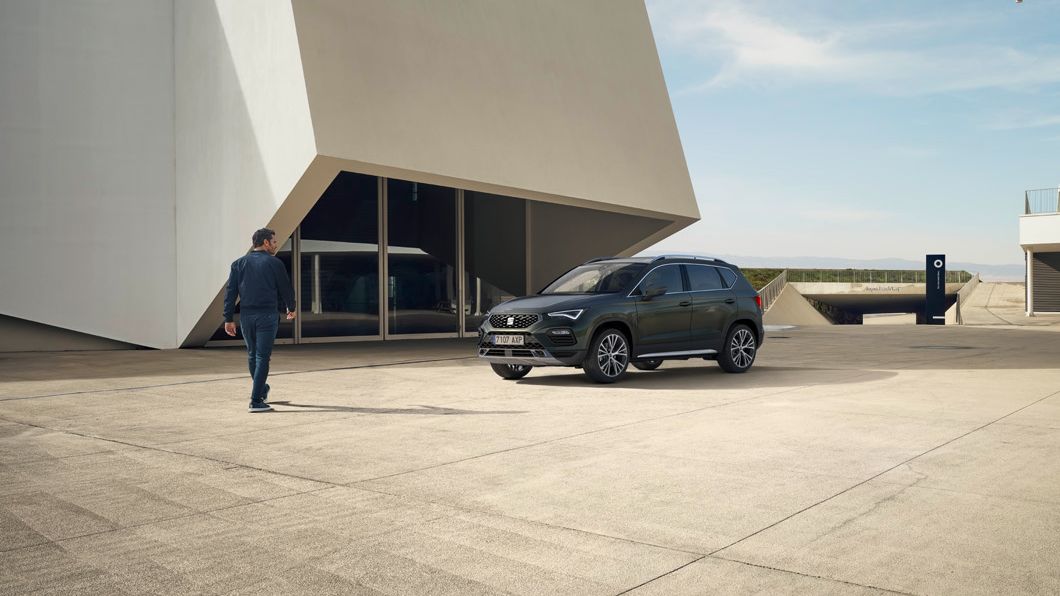 SEAT Ateca zaparkovaný pri dvoch moderných budovách. Muž prechádza okolo a pozerá sa na vozidlo. 