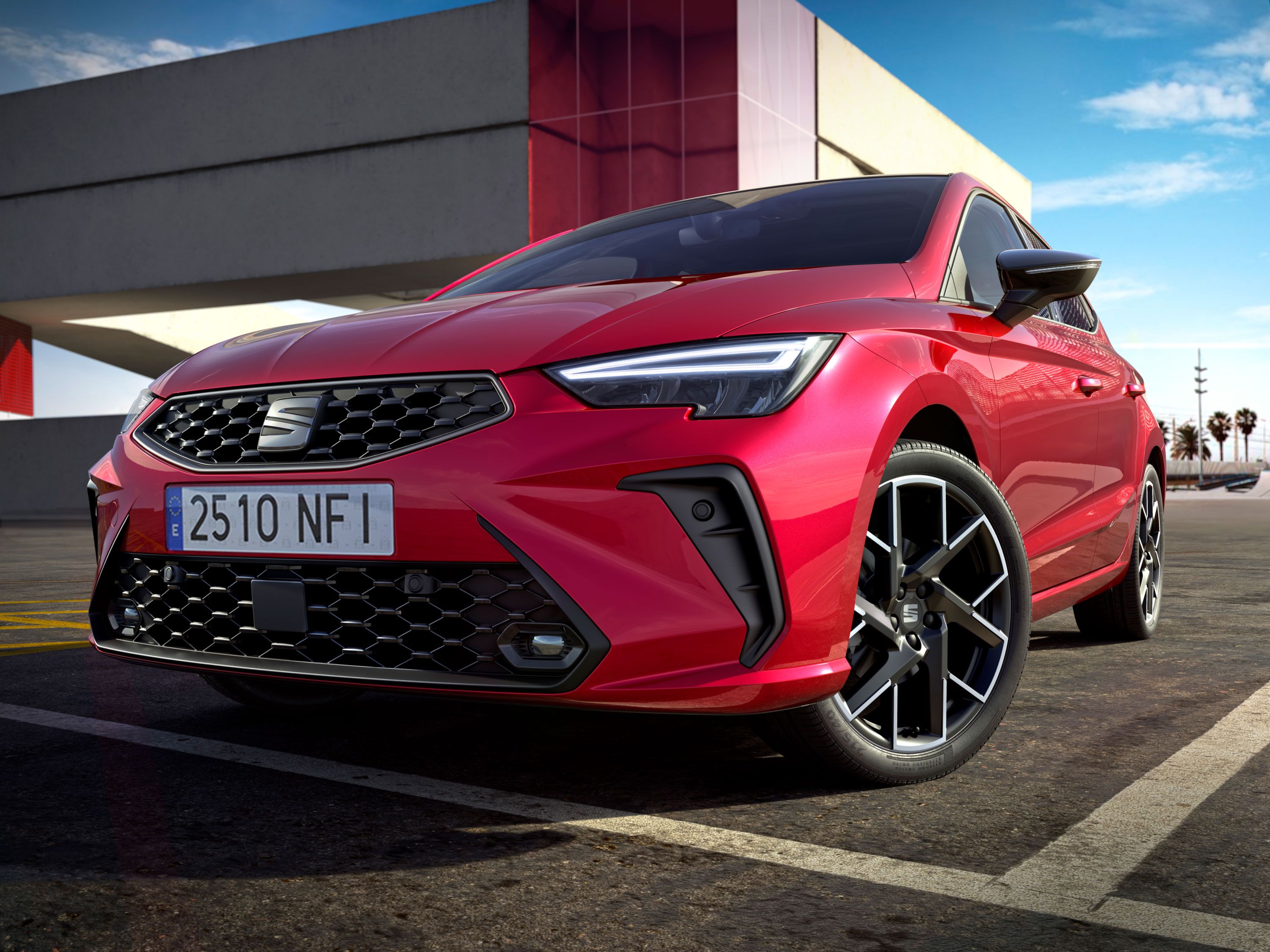 Červené auto značky Seat zaparkované pri modernom betónovom komplexe.