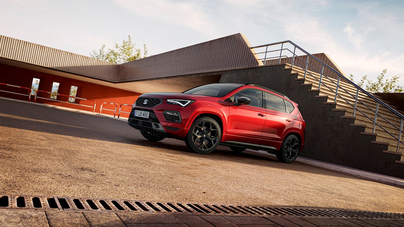 Červený model SEAT Ateca stojí na parkovisku pred modernou stavbou so schodmi na pochôdznu strechu.
