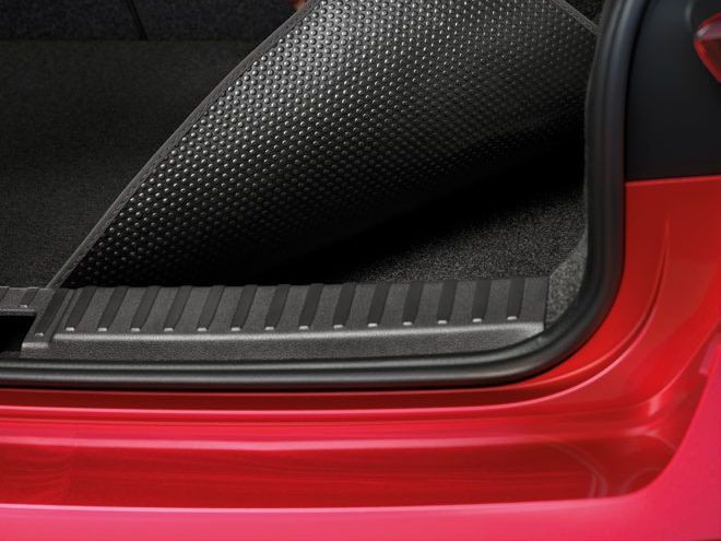 Ruka zdvíhajúca čiernu gumovú podložku v batožinovom priestore červeného auta. Batožinový priestor je prázdny a má mäkké čalúnenie.