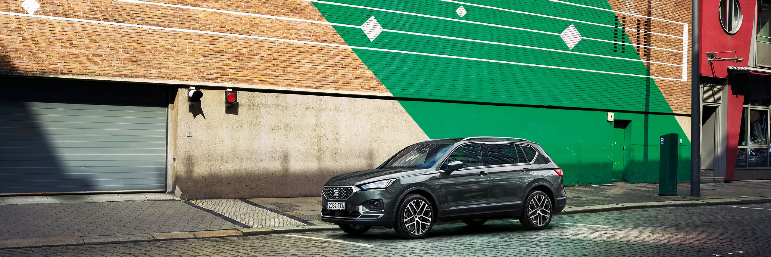 SEAT Tarraco stojí pred parkovacím domom so zeleným šikmým pruhom a bielymi pruhmi.