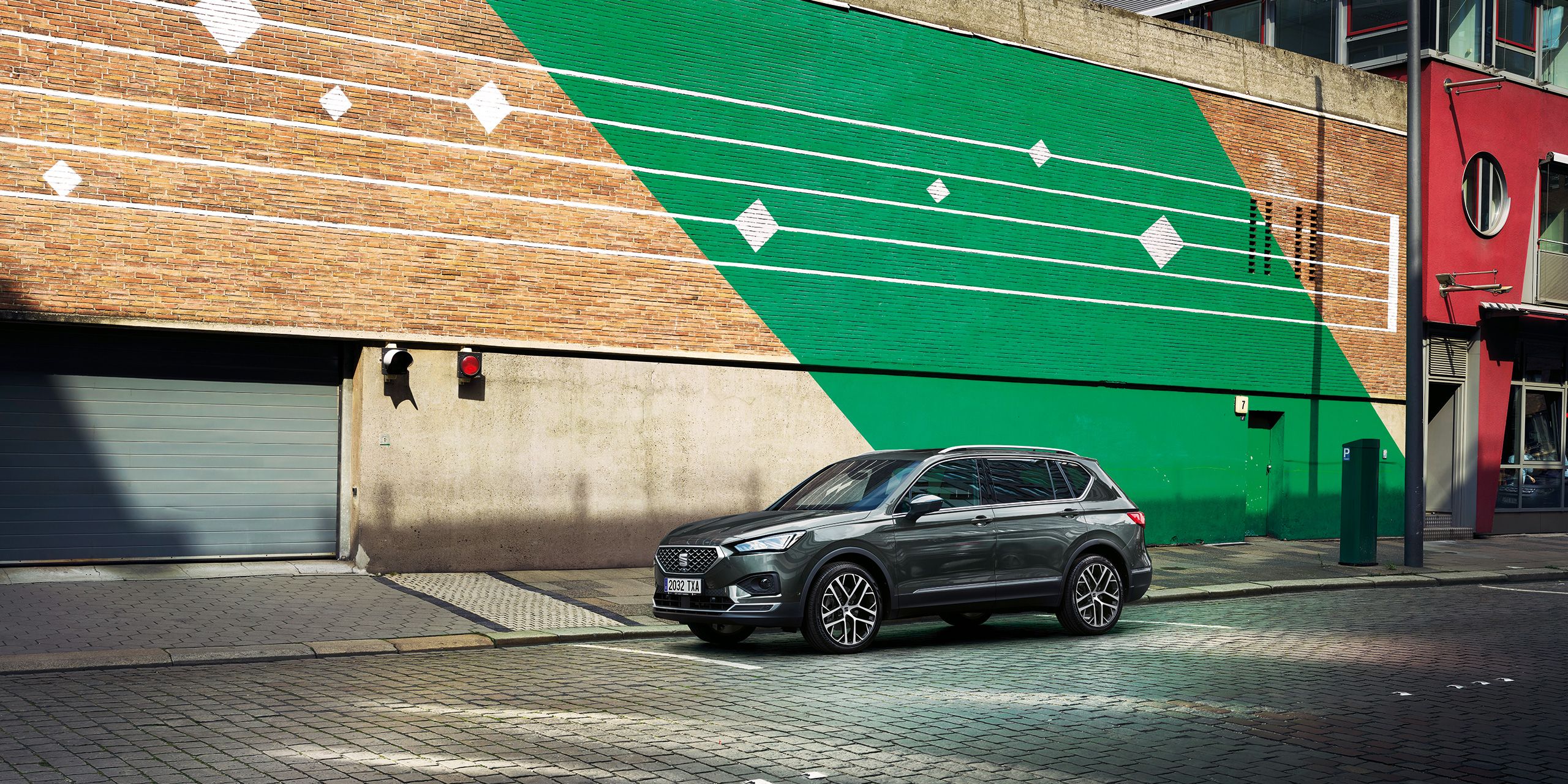 SEAT Tarraco stojí pred parkovacím domom so zeleným šikmým pruhom a bielymi pruhmi.