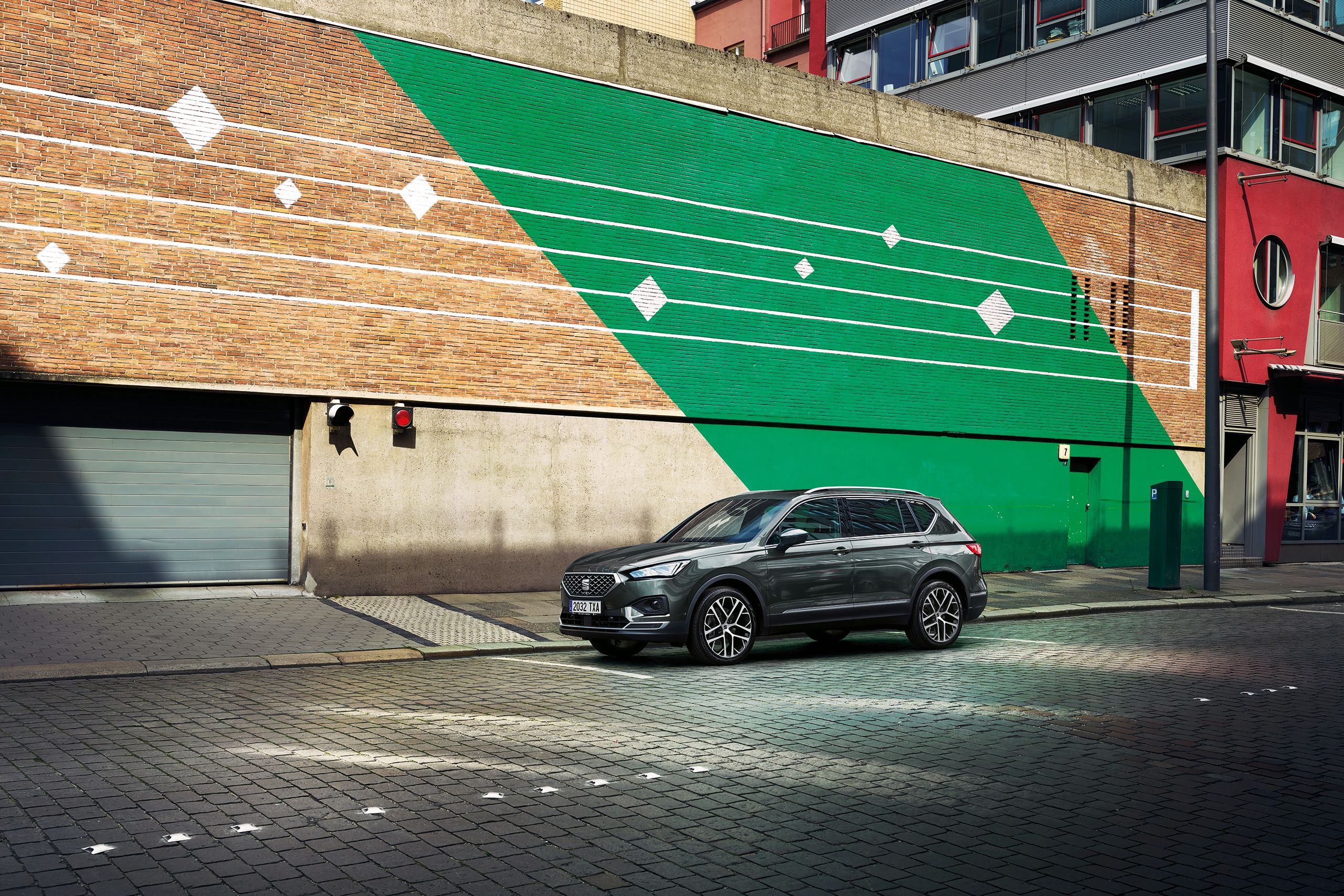 SEAT Tarraco stojí pred parkovacím domom so zeleným šikmým pruhom a bielymi pruhmi.