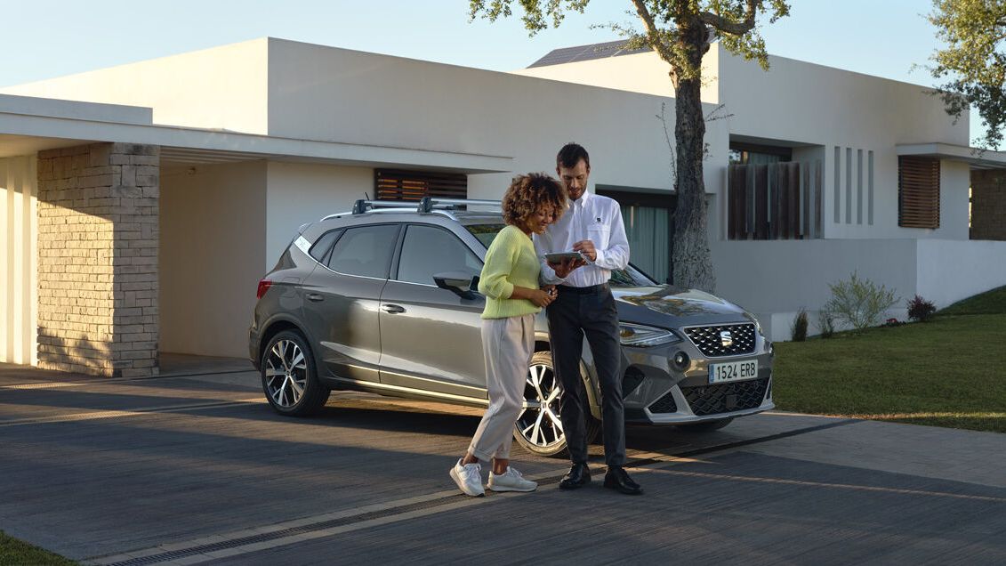 SEAT Arona je zaparkovaný pred modernou vilou. Pri vozidle stoji dvojica, muž a muž ukazuje žene niečo na tablete.