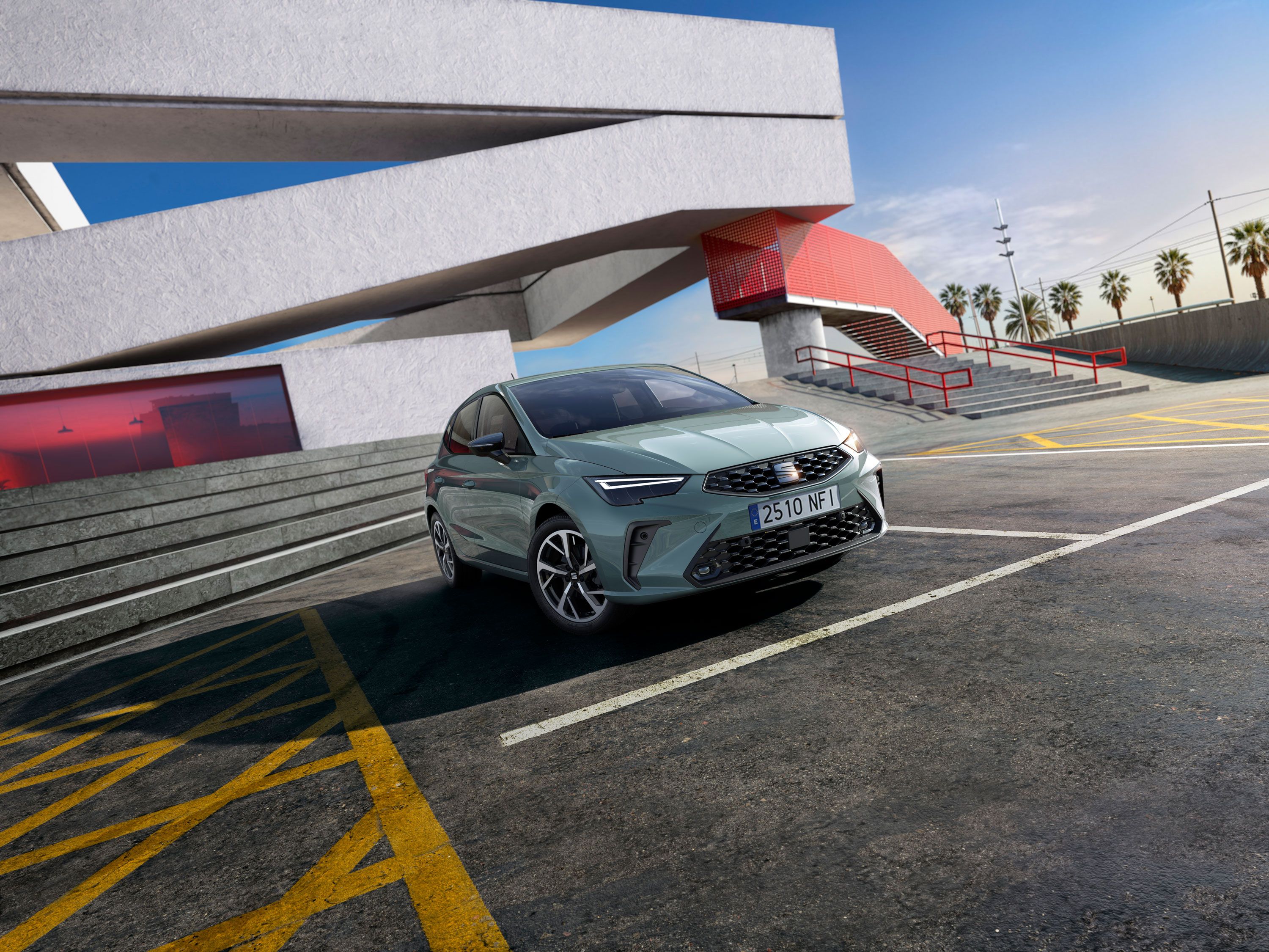 Nové svetlozelené auto značky SEAT zaparkované na parkovisku pred modernou budovou. V pozadí sú palmy a jasná obloha. Auto je umiestnené na parkovacom mieste s výraznými žltými čiarami.